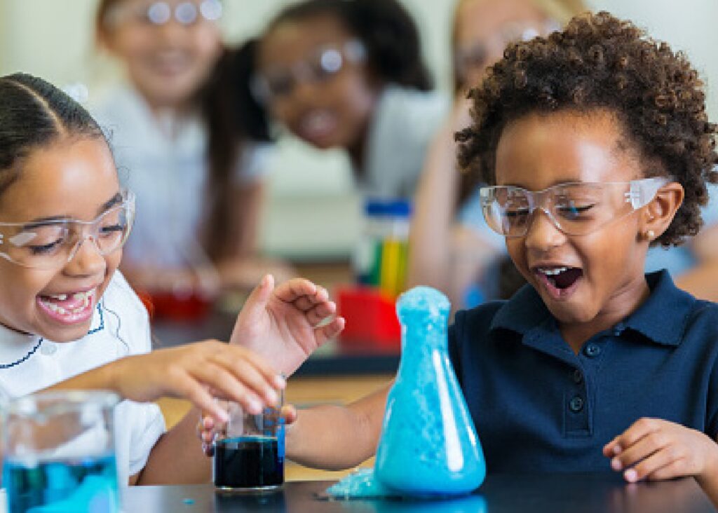 Two children laughing at blue foam bubbling up out of a glass beaker